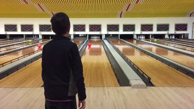 Young kid throwing bowling ball down the path to bowling pins.