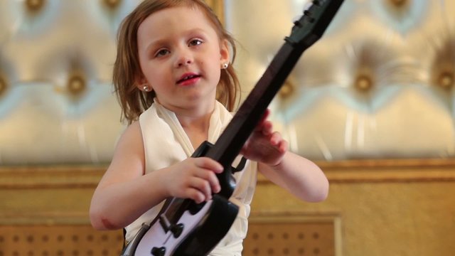 Cute small girl in white dress plays guitar at studio