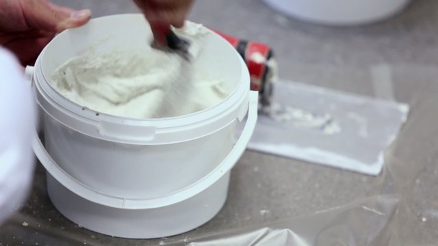 Worker in white uniform mixes putty by shovel, closeup