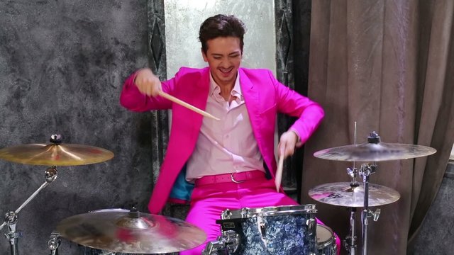 Young man in pink suit play on drum-set at dark room