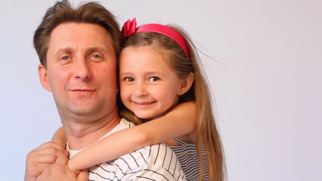 daughter embraces father from back and both smile on white