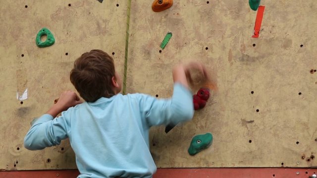 Boy-beginner tries to climb up on vertical rock-climbing wall
