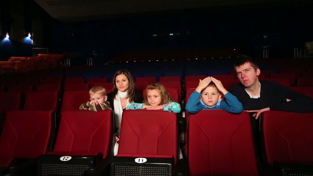 woman and man with children watching a movie in an empty cinema