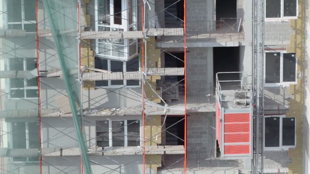 Elevator moves at wall of house with scaffold at building site