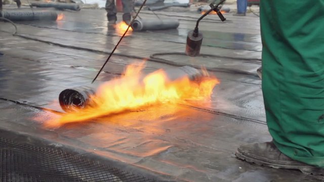 Labourers use burners to warm ruberoid for waterproofing