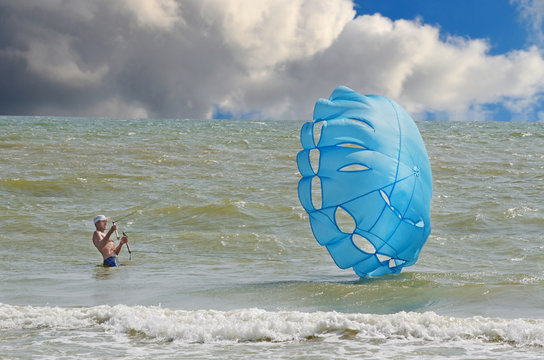 Парашютный спорт. Мужчина в море удерживает  парашют на ветру