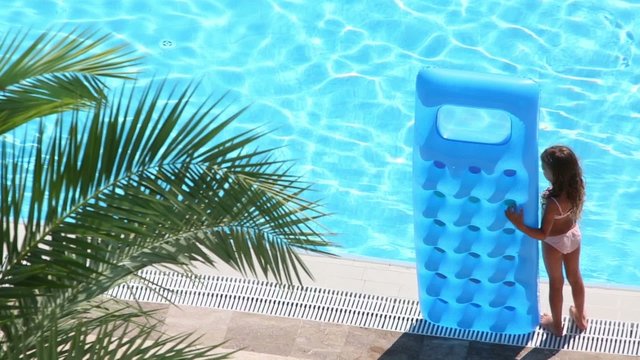 Little girl stands with inflatable mattress on edge of pool