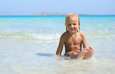 Fototapeta na wymiar Cute little smiling boy plays at tropical beach