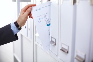 Man's hand holding big folder from the shelves with office files