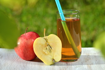 szklanka soku jabłkowego i jabłko na stole w ogrodzie - obrazy, fototapety, plakaty