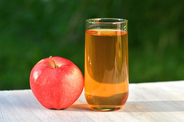 szklanka soku jabłkowego i jabłko na stole w ogrodzie