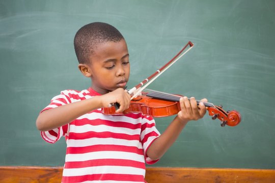 Cute african american pupil playing violin in classroom