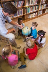 Fototapeta premium Cute pupils and teacher looking at globe in library