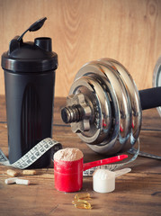 Whey protein powder in scoop with vitamins and plastic shaker