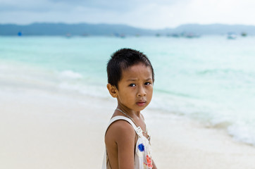 Young impoverished asian boy at exotic white beach on Boracay
