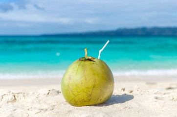 Fototapeta na wymiar Tropical green coconut with straw on exotic sandy beach