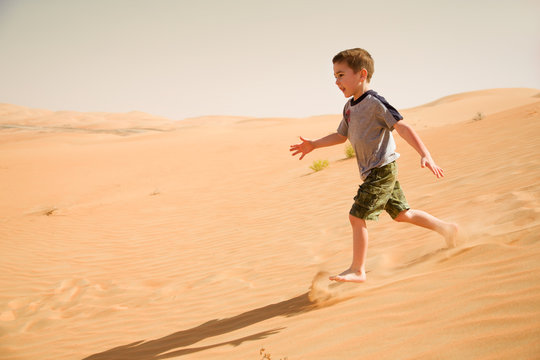 Young boy runs down in desert sand