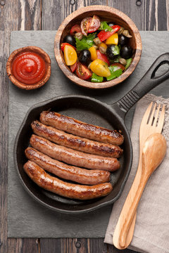 grilled sausages in a pan and vegetable salad. top view