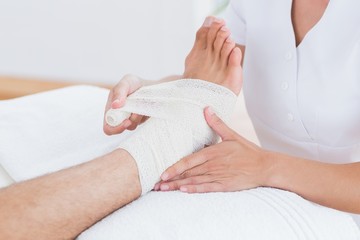 Obraz na płótnie Canvas Doctor bandaging her patient ankle