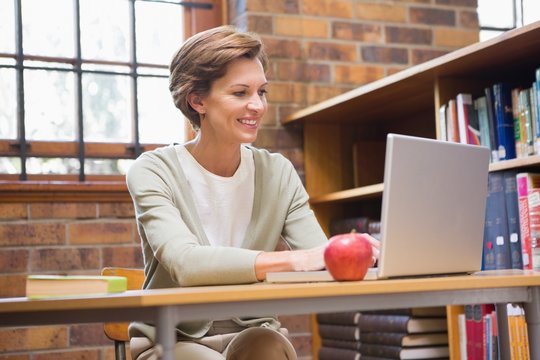Smiling teacher using laptop at a desk