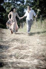 Fototapeta premium carefree Indian couple running along dirt road holding hands