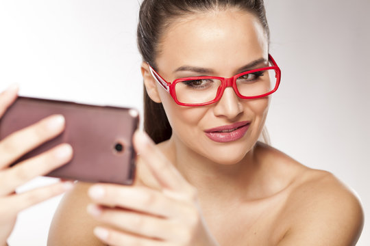 young woman with bare shoulders and red glasses make a selfie