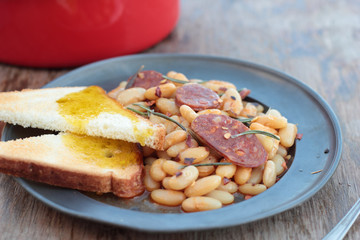 Beans and chorizo cooked with rosemary leaves on a tin plate.