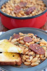 Beans and chorizo cooked with rosemary leaves on a tin plate.