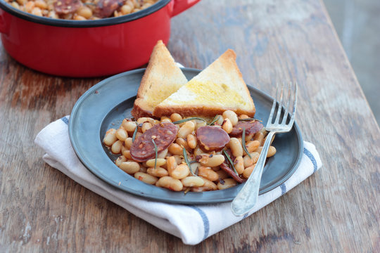 Beans and chorizo cooked with rosemary leaves on a tin plate.