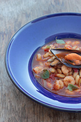 Beans and chorizo cooked with seafood on a blue plate.