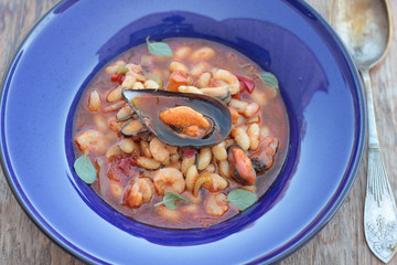 Beans and chorizo cooked with seafood on a blue plate.