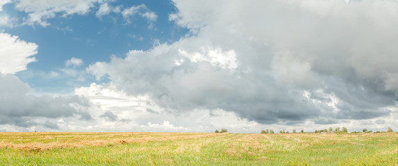 Cumulus on azure sky above harvested grain field