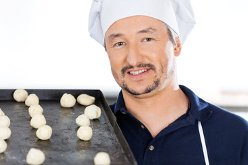 Confident Chef Carrying Baking Sheet With Dough Balls At Kitchen