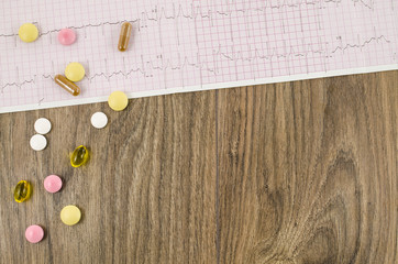Electrocardiogram with pills on wooden table