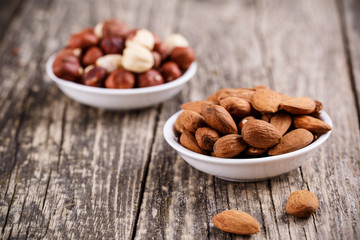 Hazelnuts and almonds on white plates.