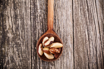Brazil nuts on a spoon on wooden background.