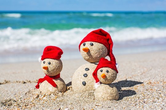 Beach. Snowmen family at sea beach in santa hats. New years and