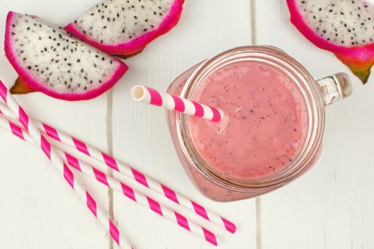 Pink smoothie with dragon fruit slices and straws on white wood