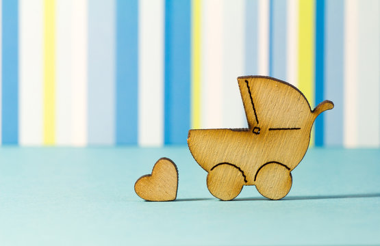Wooden icon of baby carriage and little heart on blue striped ba
