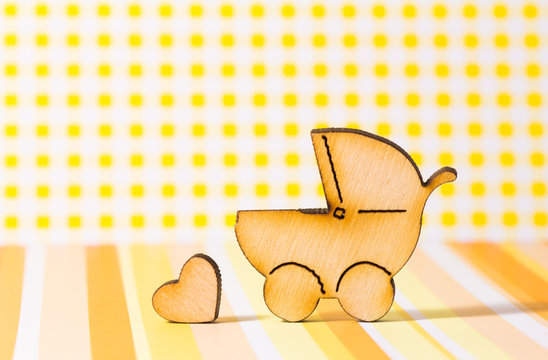 Wooden icon of baby carriage and little heart on yellow backgrou