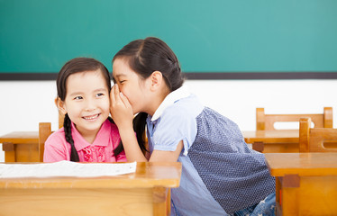 little girls whispering and sharing a secret in classroom