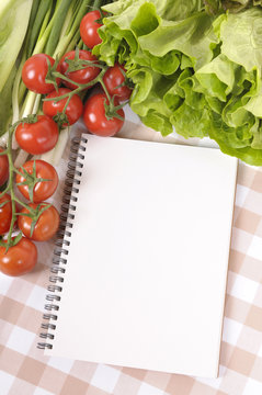 Summer salad lettuce tomato ingredients on kitchen worktop counter with blank notebook cookbook or recipe book for copy photo vertical
