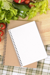 Making preparing summer salad lettuce tomato ingredients on kitchen worktop counter with blank notebook cookbook or recipe book for copy photo vertical