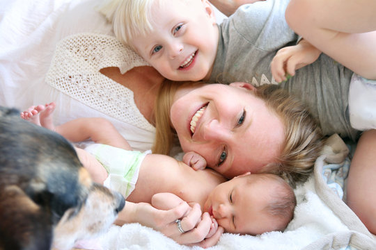 Happy Mother Laying in Bed with Toddler Son and Newborn Baby