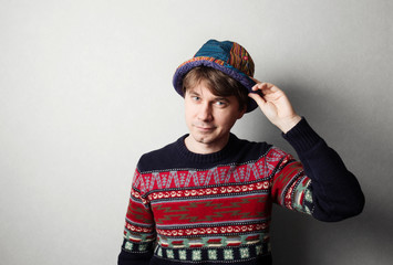 Young handsome man in knit colourful clothes, gray wall behind