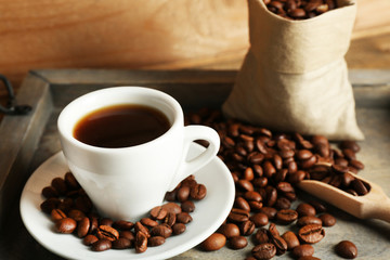 Cup of coffee with beans on tray and rustic wooden background