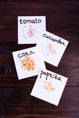 Different seeds on pieces of paper on wooden background