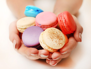 Tasty colorful macaroons in female hands isolated on white