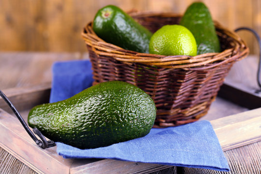 Avocado with limes in basket on wooden background