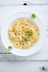 Italian tortellini in bouillon over white wooden surface